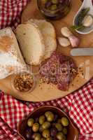 Overhead view of chili flakes on meat by bread with olives in jar
