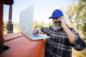Man using laptop while talking on mobile phone