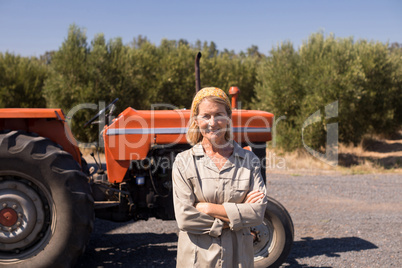 Portrait of happy woman standing with arms crossed against tractor