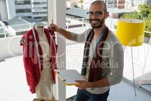 Portrait of smiling designer holding clipboard standing by mannequin