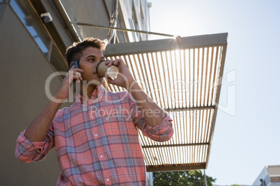 Low angle view of man having drink while talking on mobile phon