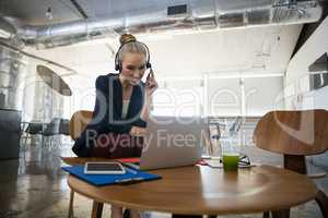 Businesswoman talking through headset while using laptop