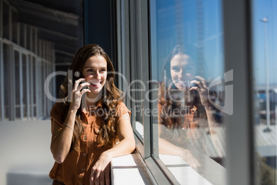 Smiling businesswoman talking on mobile phone by window at office