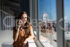 Smiling businesswoman talking on mobile phone by window at office