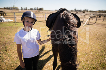 Smiling girl standing next to the brown horse in the ranch