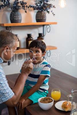 Grandfather feeding grandson sitting on table