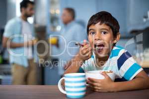 Portrait of boy having breakfast with family in background