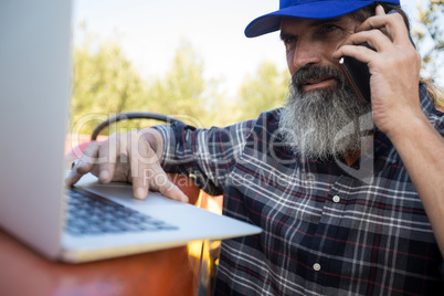 Man using laptop while talking on mobile phone