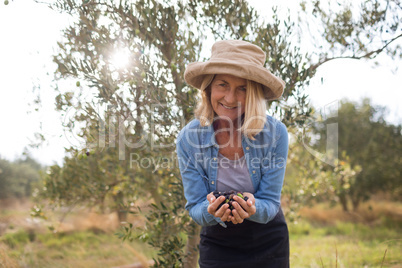 Portrait of happy woman holding harvested olives in farm