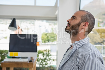 Thoughtful designer looking up while leaning on glass window