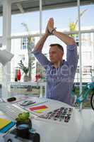 Designer with arms raised meditating while sitting at desk
