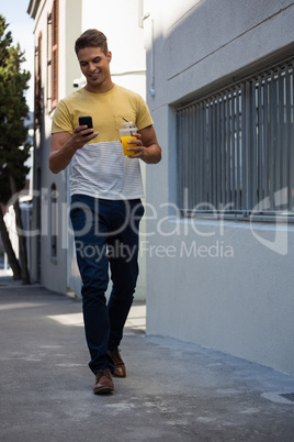Young man having juice while using mobile phone