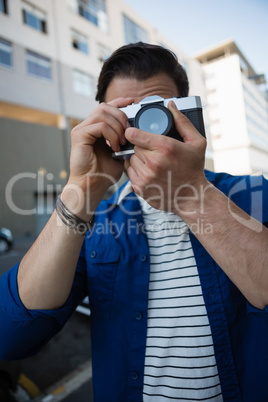 Man photographing through camera while standing by building