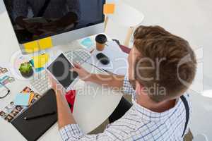 Graphic designer using tablet computer while sitting at desk in studio