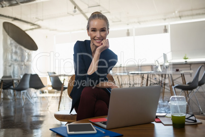 Portrait of smiling businesswoman with hand on chin sitting in office