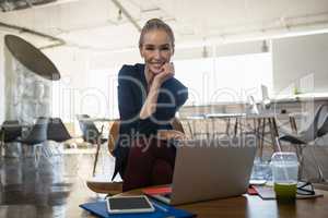 Portrait of smiling businesswoman with hand on chin sitting in office