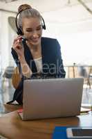 Businesswoman talking through headset while using laptop