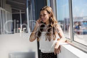 Smiling businesswoman talking on phone while standing by window