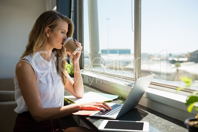 Businesswoman drinking coffee while using laptop