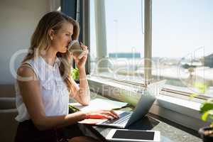 Businesswoman drinking coffee while using laptop