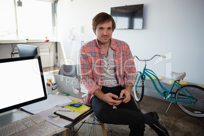 Portrait of man using phone while sitting on desk at office