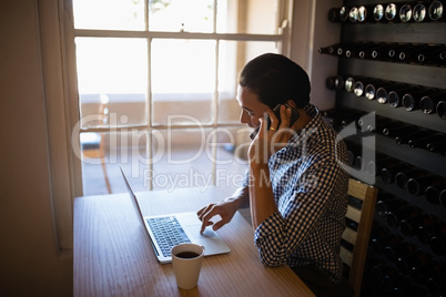 Man using laptop while talking on mobile phone