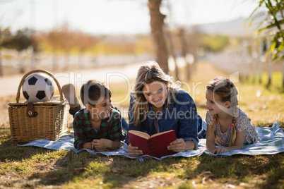 Mother and kids reading novel in park