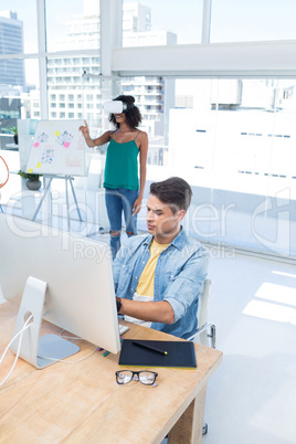 Male executive working on computer while female executive using virtual reality headset