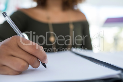 Female executive writing on a document at desk in the office