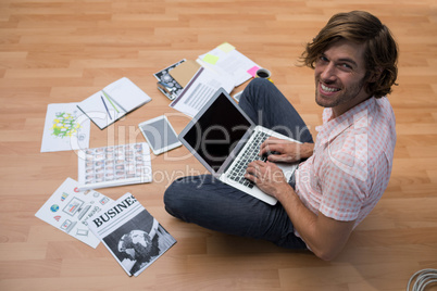 Male executive using laptop while sitting on floor in the office