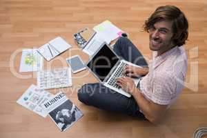 Male executive using laptop while sitting on floor in the office