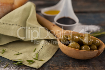 Green olives in spoon with oil on table