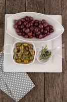 Brown and green olives by rosemary on plate