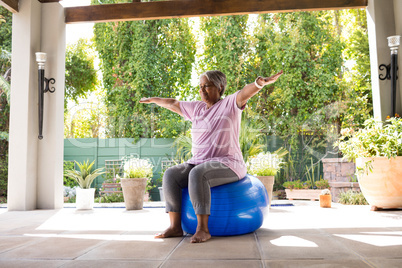 Senior woman with arms outstretched sitting on exercise ball