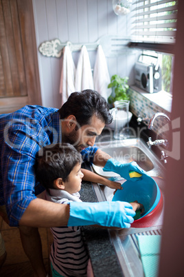 Father assisting son for cleaning utensils at home