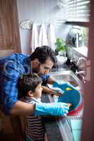 Father assisting son for cleaning utensils at home