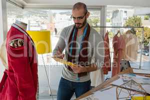 Designer writing on paper while standing by mannequin