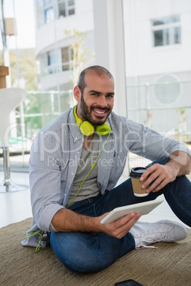 Portrait of designer holding disposable cup and tablet computer while sitting on floor