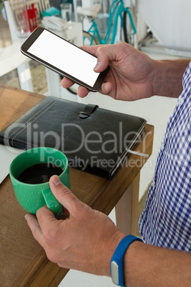 Designer using mobile phone while holding drink at table