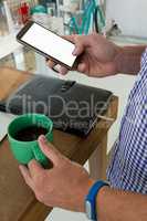 Designer using mobile phone while holding drink at table