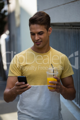 Smiling young man having juice while using mobile phone