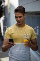 Smiling young man having juice while using mobile phone