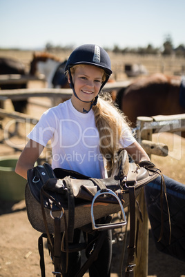 Smiling girl holding horse saddle