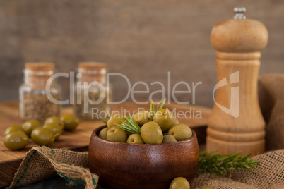 Olives and rosemary in bowl by pepper shaker