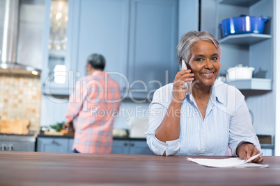 Portrait of smiling woman talking phone while standing in kitchen