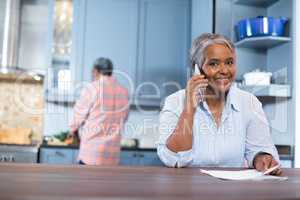 Portrait of smiling woman talking phone while standing in kitchen