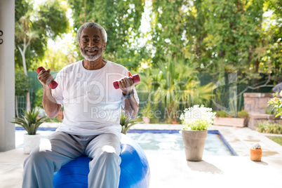 Portrait of man holding dumbbells while sitting on fitness ball