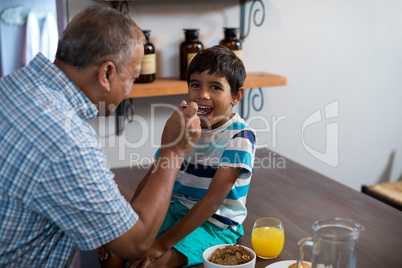 Happy grandfather feeding grandson sitting on table