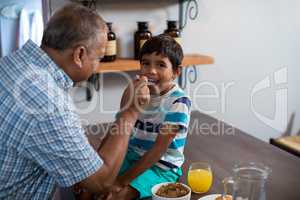 Happy grandfather feeding grandson sitting on table