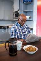 Smiling man reading newspaper while having breakfast